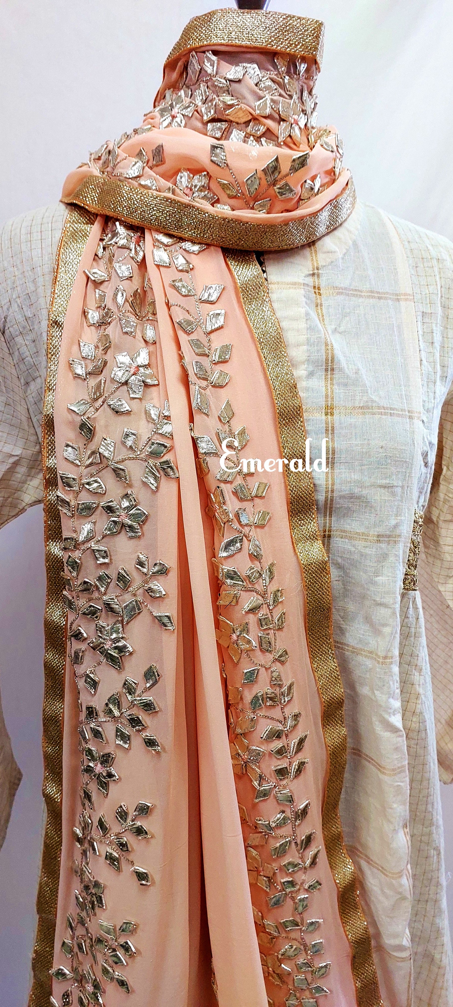 An elegant,embroidered peach Dupatta in georgette. Dupatta is bordered with a broad patch of silver gota patti work and butis in the middle area.Trimmed with an antique gold border. Perfect for any events in the wedding season!Dupatta measurements:Length-2.4mWidth-39inWash Care- Dry Clean Only.